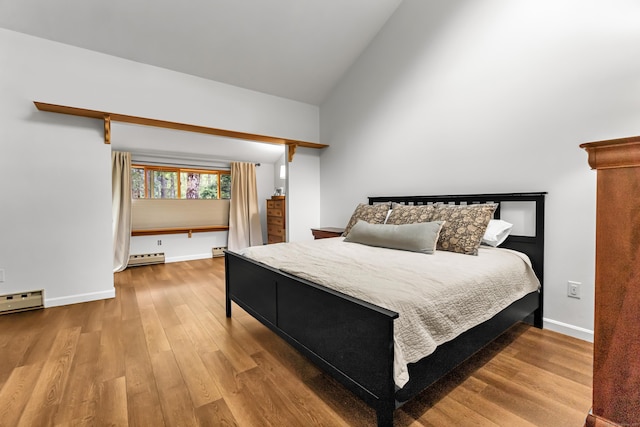 bedroom with vaulted ceiling, a baseboard heating unit, baseboards, and wood finished floors