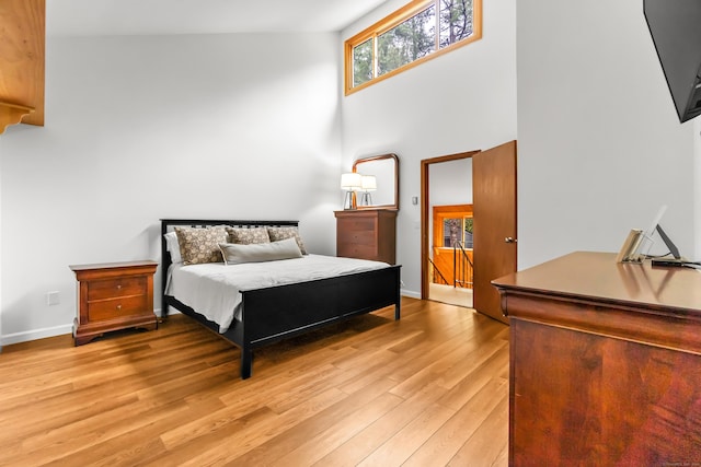 bedroom featuring a towering ceiling, baseboards, and light wood-type flooring