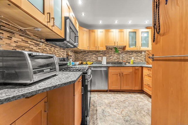 kitchen with dark stone counters, glass insert cabinets, decorative backsplash, and stainless steel appliances
