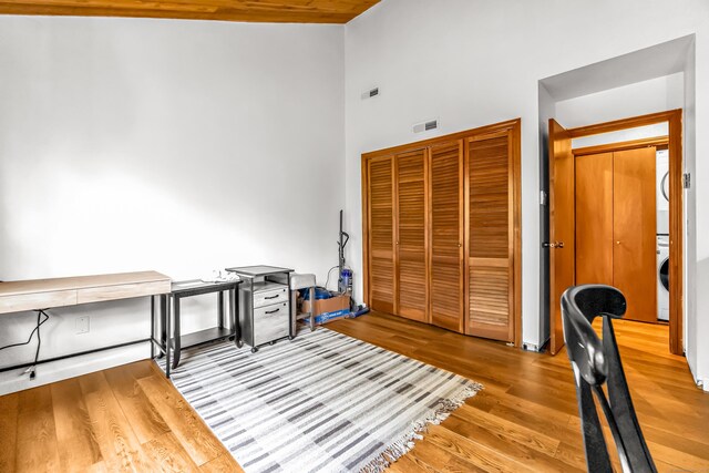 office with stacked washer / dryer, visible vents, a towering ceiling, and wood finished floors