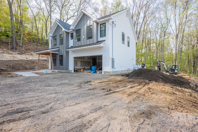 exterior space featuring a garage, a standing seam roof, dirt driveway, board and batten siding, and metal roof