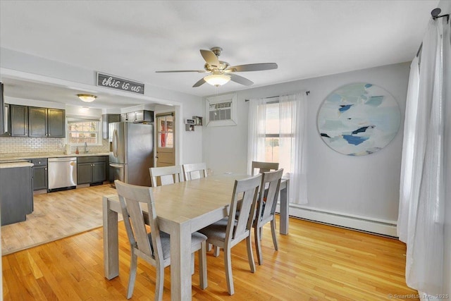 dining room with a ceiling fan, a wealth of natural light, light wood-style flooring, and a baseboard radiator