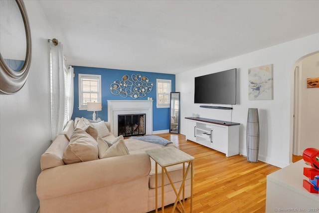 living room with arched walkways, a brick fireplace, light wood finished floors, and a wealth of natural light