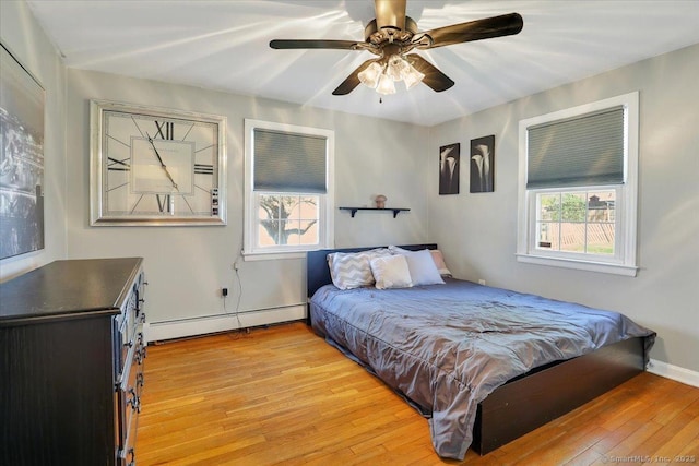 bedroom with a baseboard radiator, a ceiling fan, multiple windows, and light wood-style flooring