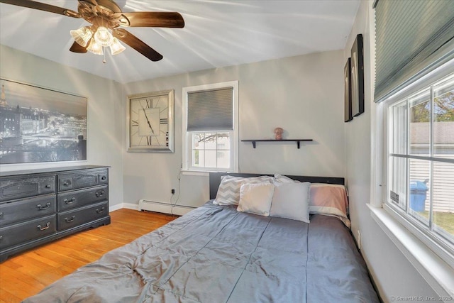 bedroom featuring a baseboard heating unit, ceiling fan, wood finished floors, and multiple windows