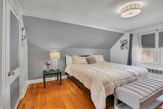 bedroom with baseboards, radiator heating unit, lofted ceiling, and light wood-type flooring