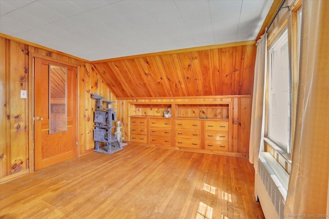 additional living space with radiator, wood walls, light wood-style flooring, and lofted ceiling