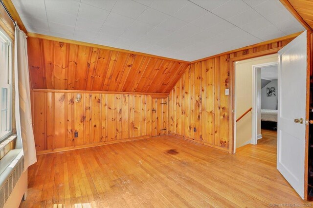 additional living space with radiator heating unit, wood walls, baseboards, and light wood finished floors