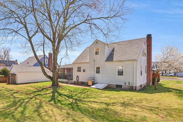 rear view of property featuring a sunroom, a shingled roof, a yard, and a chimney