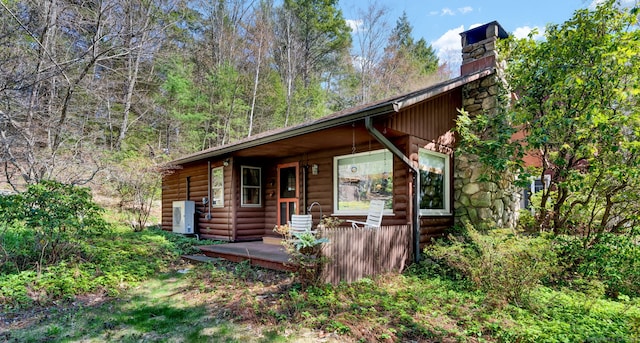 view of front of house featuring covered porch, log veneer siding, and a chimney