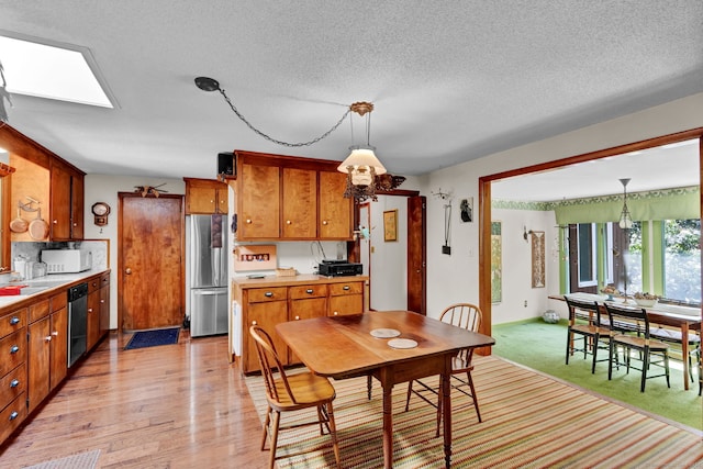 kitchen featuring appliances with stainless steel finishes, light countertops, brown cabinetry, decorative light fixtures, and a skylight