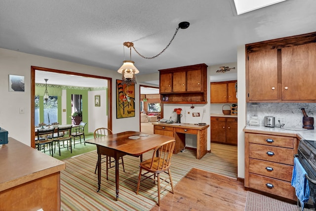 kitchen with light countertops, brown cabinets, tasteful backsplash, range, and decorative light fixtures