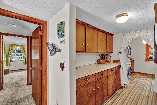 washroom featuring stacked washer and dryer, a textured ceiling, light carpet, and baseboards