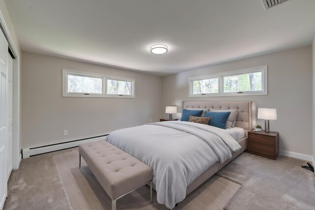 bedroom featuring light carpet, visible vents, baseboards, a baseboard heating unit, and a closet