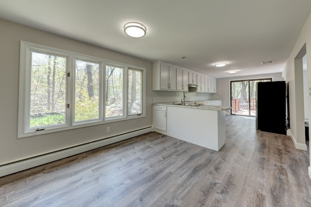 kitchen featuring visible vents, baseboard heating, light countertops, a peninsula, and light wood-style flooring