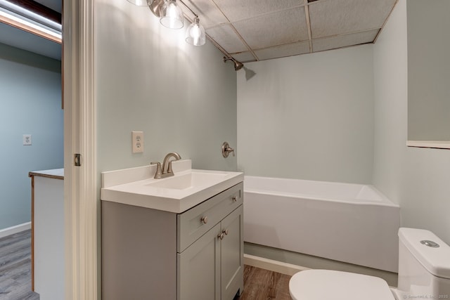 bathroom featuring vanity, toilet, a drop ceiling, bathing tub / shower combination, and wood finished floors