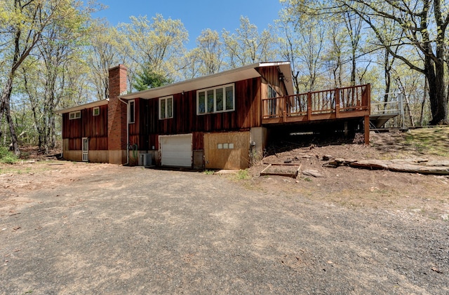 view of home's exterior featuring a garage, a deck, a chimney, central AC unit, and driveway