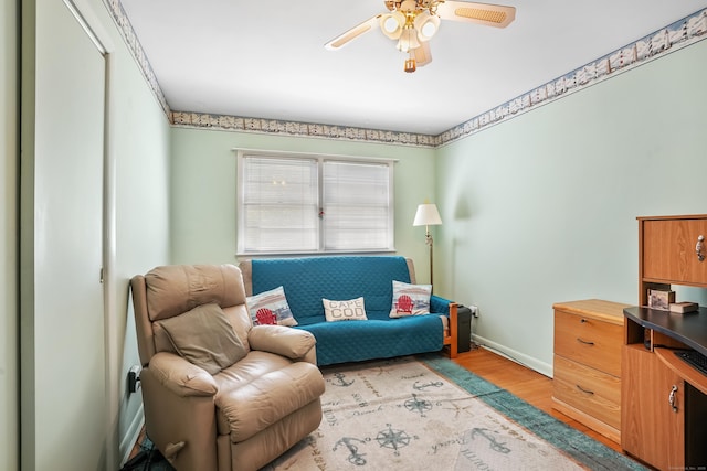 living area with baseboards, a ceiling fan, and light wood finished floors
