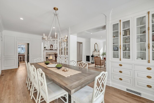 dining space with a decorative wall, a lit fireplace, light wood-type flooring, and a chandelier