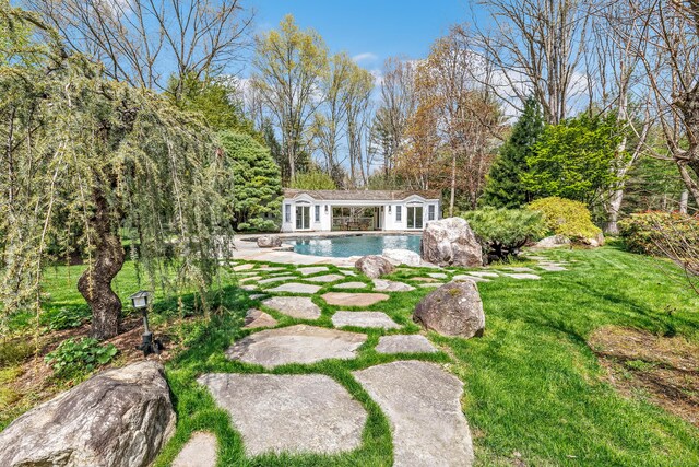 view of yard with an outbuilding, an outdoor pool, a patio area, an exterior structure, and a view of trees