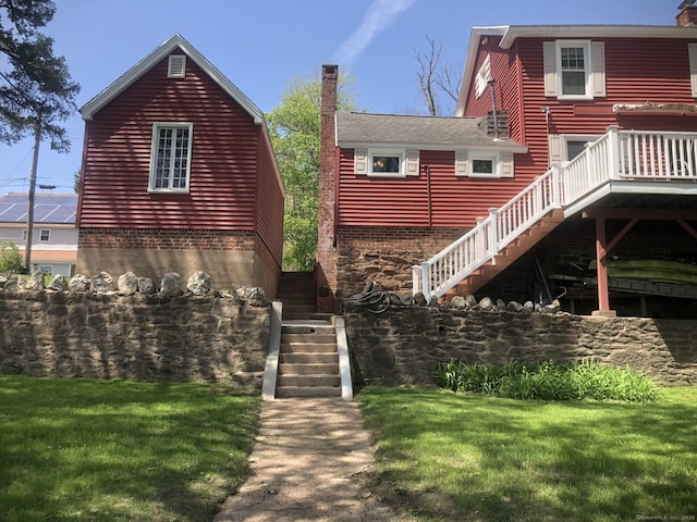 back of house featuring stairs, a lawn, and a chimney