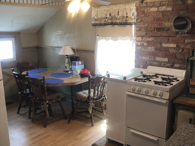 kitchen with white gas stove, ceiling fan, wood finished floors, and a wainscoted wall