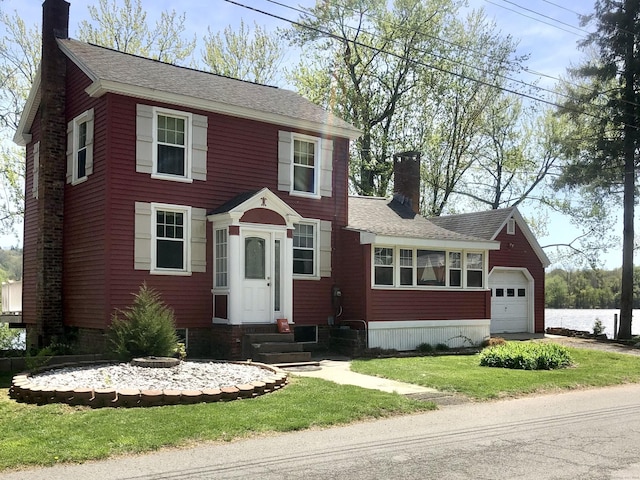 colonial-style house with a shingled roof, a garage, a front yard, entry steps, and a chimney