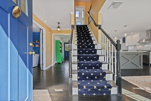 stairway featuring baseboards, visible vents, ornamental molding, and wood finished floors