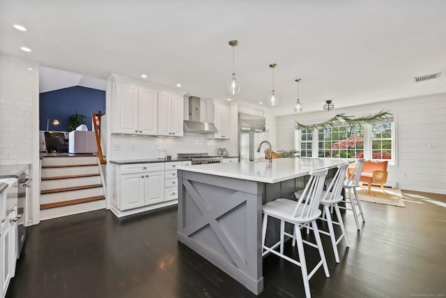kitchen featuring white cabinets, a kitchen breakfast bar, wall chimney exhaust hood, visible vents, and dark wood-style floors
