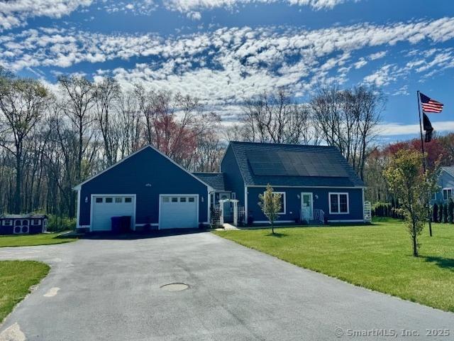 single story home with roof mounted solar panels, an attached garage, driveway, and a front yard
