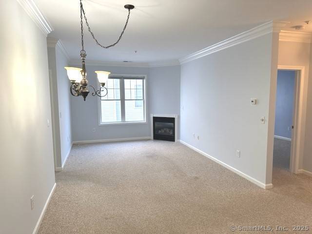 unfurnished living room featuring crown molding, carpet floors, baseboards, and a chandelier