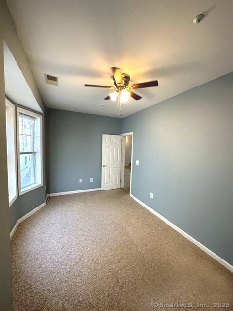 carpeted spare room featuring baseboards, ceiling fan, and visible vents