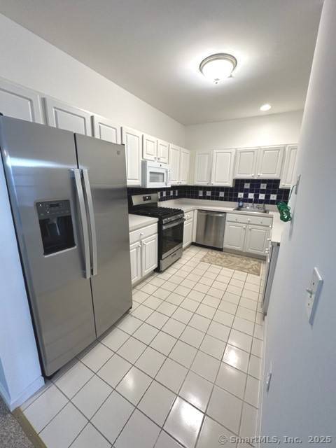 kitchen featuring a sink, appliances with stainless steel finishes, light tile patterned floors, and white cabinets