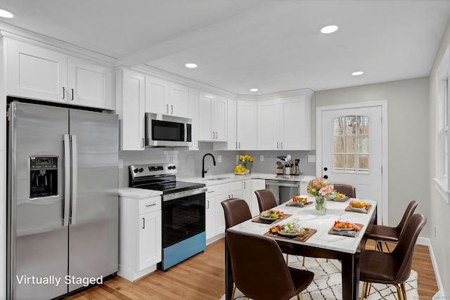 kitchen with a sink, light wood-style floors, light countertops, stainless steel appliances, and white cabinetry