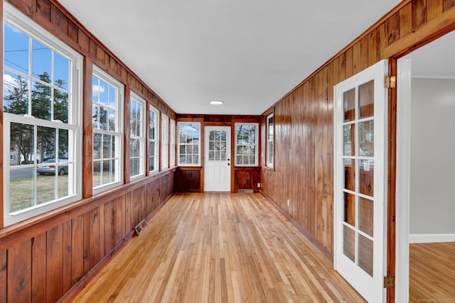 unfurnished sunroom featuring crown molding, wood-type flooring, wood walls, baseboards, and visible vents