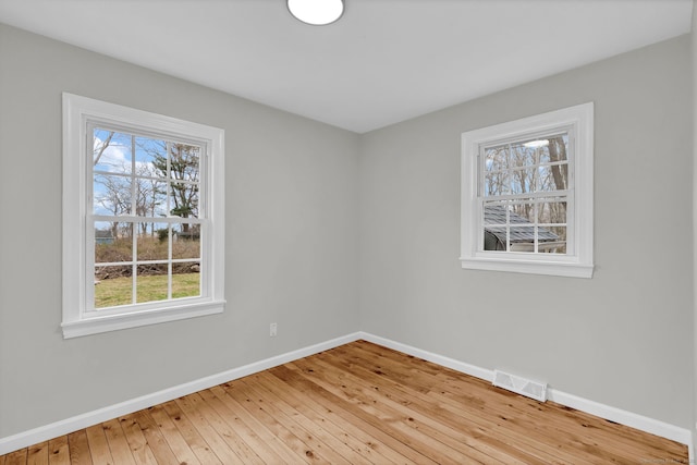 empty room featuring a healthy amount of sunlight, baseboards, hardwood / wood-style floors, and visible vents