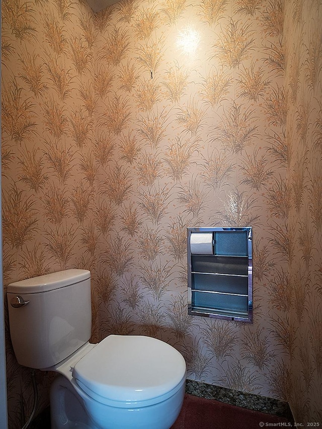 half bath featuring baseboards, toilet, and wallpapered walls