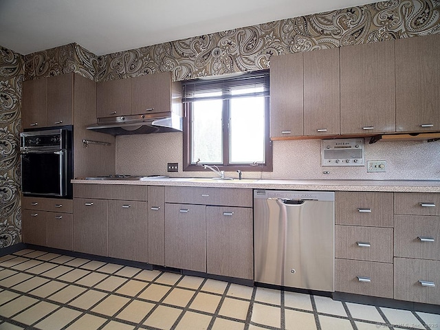 kitchen featuring oven, light floors, light countertops, under cabinet range hood, and dishwasher