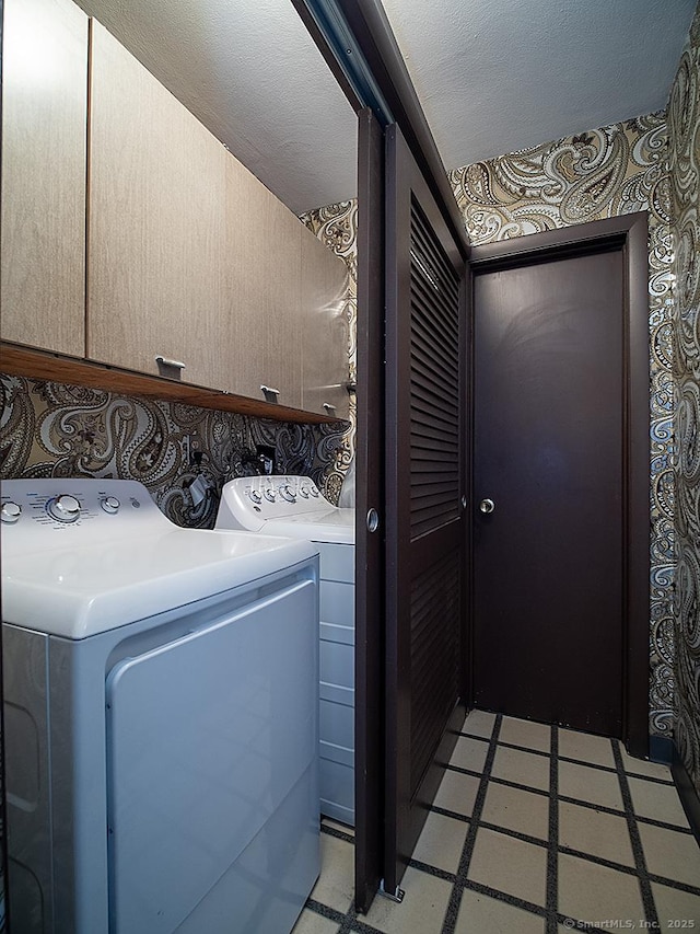 laundry area featuring washing machine and clothes dryer, cabinet space, a textured ceiling, wallpapered walls, and light floors