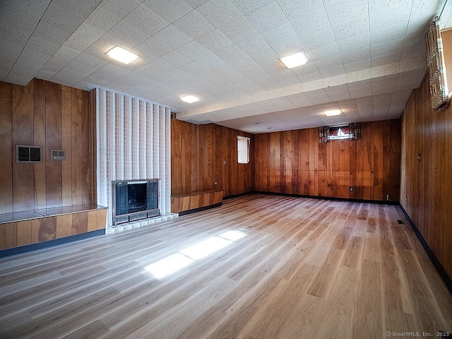finished basement featuring visible vents, wood walls, a brick fireplace, and wood finished floors