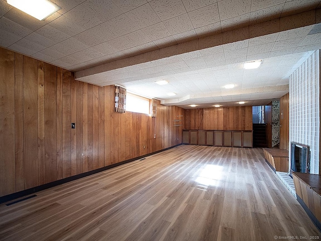 below grade area featuring wood walls, visible vents, and light wood-style floors