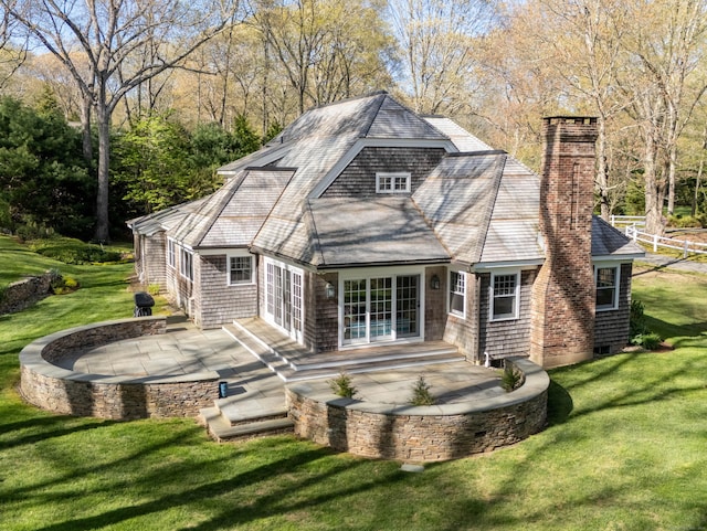 rear view of property featuring a chimney, a patio area, a shingled roof, and a lawn
