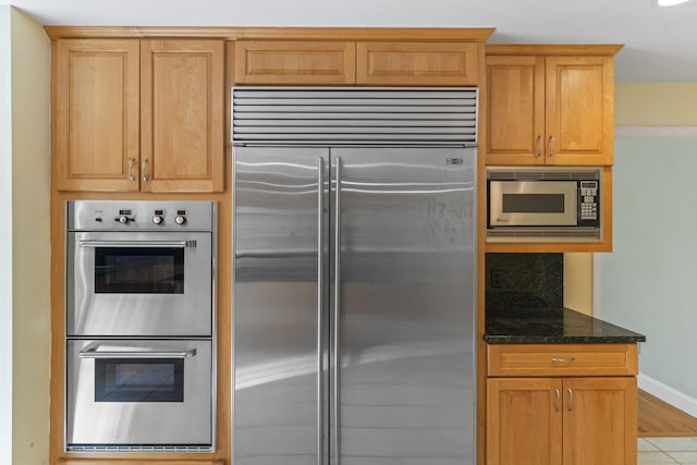 kitchen featuring built in appliances, baseboards, and dark stone countertops