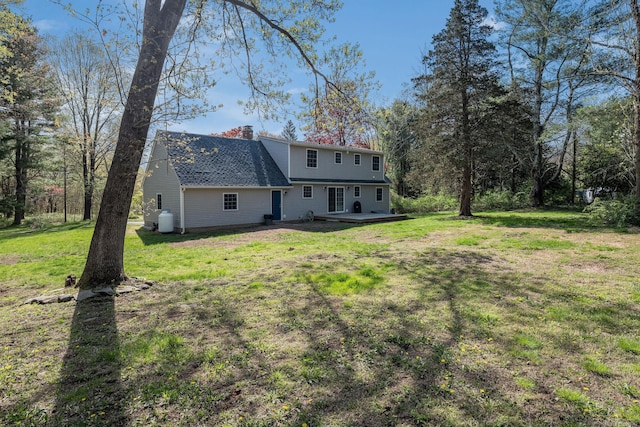 rear view of property featuring a yard, a chimney, and roof with shingles