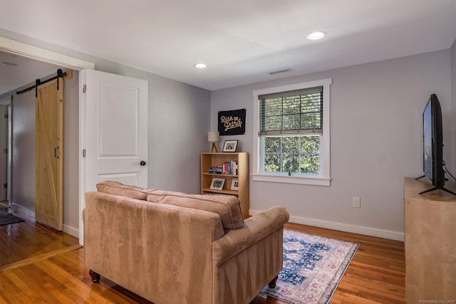 living room featuring visible vents, wood finished floors, baseboards, recessed lighting, and a barn door