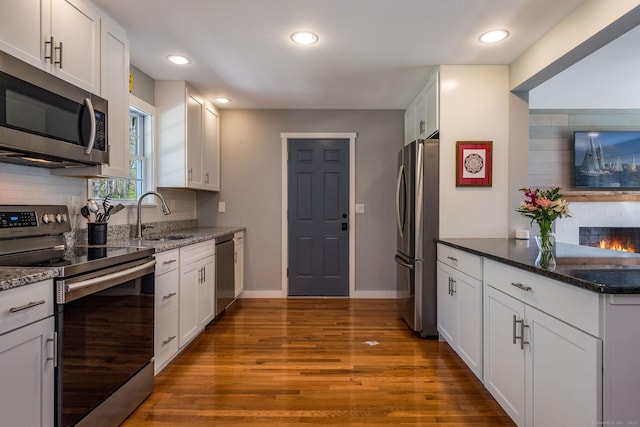 kitchen featuring wood finished floors, a sink, white cabinets, dark stone countertops, and stainless steel appliances