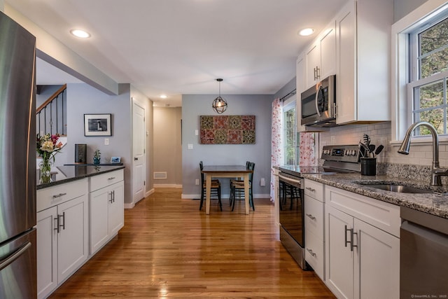 kitchen featuring appliances with stainless steel finishes, tasteful backsplash, a sink, light wood-style floors, and white cabinetry