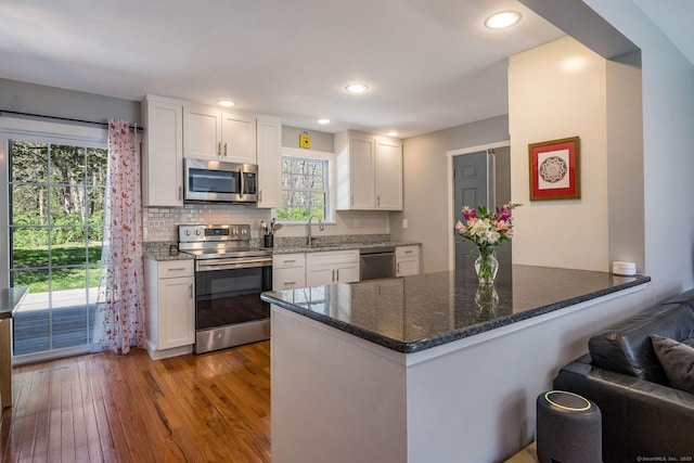 kitchen with backsplash, white cabinets, wood-type flooring, a peninsula, and stainless steel appliances