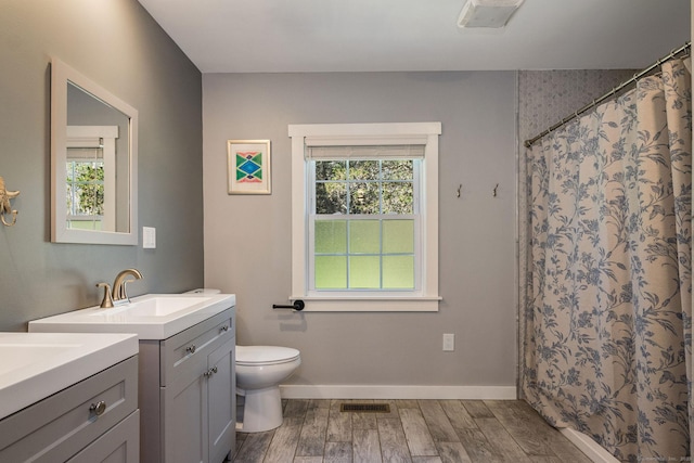 bathroom with toilet, baseboards, two vanities, wood finished floors, and visible vents