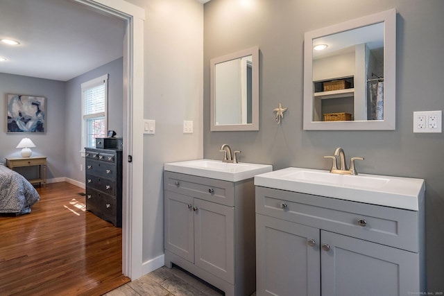 full bathroom featuring baseboards, a sink, wood finished floors, and two vanities